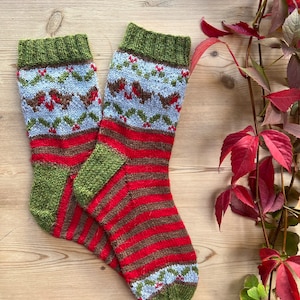 Könnte beinhalten: Ein Paar gestrickte Socken mit einem rot-grün-braunen Streifenmuster. Die Socken haben oben ein Rotkehlchen- und Stechpalmen-Design.