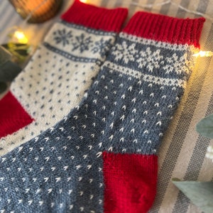 May include: A pair of knitted socks in a red, white and blue colour scheme. The socks feature a snowflake pattern and a textured design.