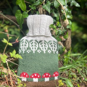 May include: A knitted hot water bottle cover with a green and white forest design and a brown bottom with red and white mushrooms.