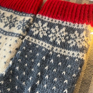 May include: A pair of knitted wool socks with a grey and white snowflake pattern and red cuffs.