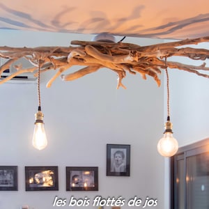 Peut inclure: Un luminaire unique en bois flotté, avec quatre ampoules suspendues de style Edison. Le luminaire est monté au plafond et a une esthétique naturelle et rustique. Le texte "les bois flottés de jos" est visible.