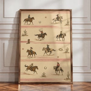 May include: A framed wall art print featuring a repeating pattern of cowboys and cowgirls riding horses across a beige background with horizontal pink stripes. The illustration includes cacti, lassos, horseshoes, and stars in a western motif.