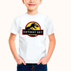May include: White t-shirt featuring a black dinosaur graphic and the text "Birthday Boy" in a red box.
