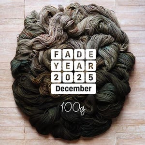 以下が含まれることがあります： 緑、茶色、グレーの色合いの手染め糸の束。白で「FADE YEAR 2025 December」と「100g」の文字。明るい木材の表面に円形に配置された糸。