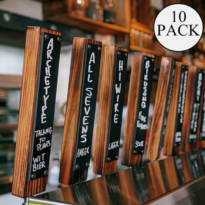 May include: Ten wooden beer tap handles with black chalkboard inserts. The handles are labeled with different beer names, including "Archetype", "All Sevens", "HiWire", "Birdsong", and "Pink Robos".
