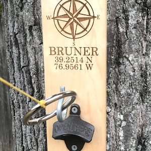 May include: Wooden sign with a compass rose, the name "BRUNER", coordinates "39.2514 N 76.9561 W", and a bottle opener. A ring toss game is attached to the sign.