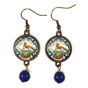May include: A pair of dangle earrings with a blue glass bead and a round pendant featuring a fox on a blue and white patterned tile design.