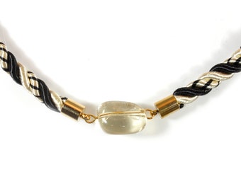 May include: A black and cream braided rope necklace with a clear quartz pendant and gold accents.