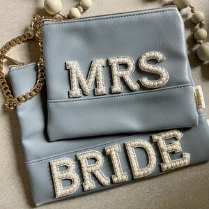 Könnte beinhalten: Zwei graue Clutch-Taschen mit perlenbesetzter Beschriftung. Die obere Tasche sagt "MRS" und die untere Tasche sagt "BRIDE".