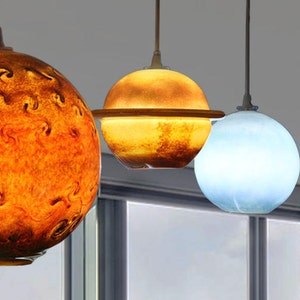 Może przedstawiać: Cztery sferyczne lampy wiszące w różnych kolorach. Pierwsza jest pomarańczowa ze wzorem wirowym, druga jest żółta z brązowym paskiem, trzecia jest jasnoniebieska, a czwarta głęboko niebieska. Każda wisi na ciemnym kablu.