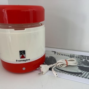 May include: A vintage SEB Fromagère cheese maker with a red lid and base, and a white body. The appliance has the SEB logo and the word "Fromagère" printed on the front. A manual and power cord are also visible.