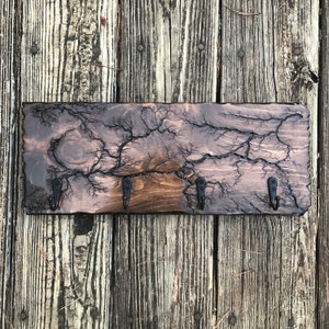 May include: A wooden key holder with a dark brown finish and a unique crackled pattern. It features four black metal hooks for hanging keys.