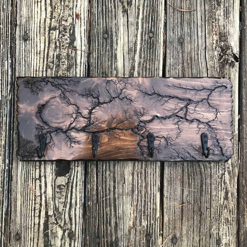 May include: A wooden key holder with a dark brown finish and a unique crackled pattern. It features four black metal hooks for hanging keys.