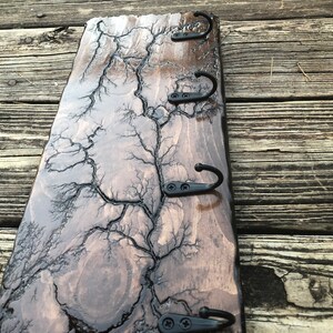 May include: A wooden key rack with a dark brown stain and a unique lightning bolt pattern. The rack has four black metal hooks.