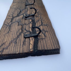May include: A wooden wall-mounted coat rack with four black metal hooks. The wood has a dark brown stain and a unique crackled finish.