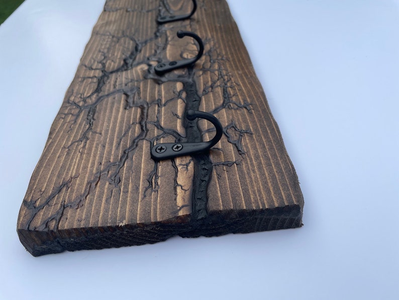May include: A wooden wall-mounted coat rack with four black metal hooks. The wood has a dark brown stain and a unique crackled finish.