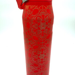 May include: A red insulated water bottle with a gold mandala pattern. The bottle has a flip-top lid and a handle. The bottle is approximately 10 inches tall.