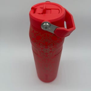 May include: A red insulated water bottle with a matching lid and handle. The bottle features a gold floral pattern and a stainless steel hinge. The lid has a flip-top closure for easy access. The bottle is designed to keep beverages cold or hot.