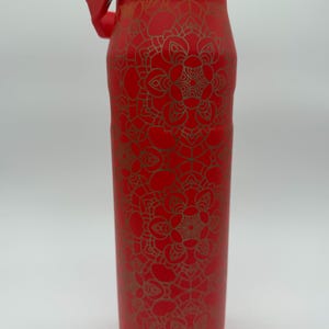 May include: A red insulated water bottle with a gold mandala pattern. The bottle has a red lid with a silver hinge and handle. The bottle is approximately 10 inches tall.