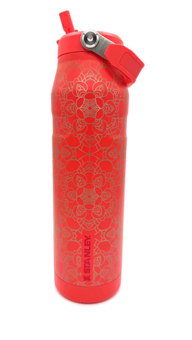 May include: Red insulated water bottle with a gold mandala pattern. The bottle has a red lid with a flip-top straw and a metal handle. The Stanley logo is visible on the side.