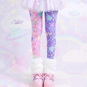 May include: A whimsical outfit featuring split-color leggings, one leg pink and the other purple, adorned with heart and sprinkle patterns. The ensemble includes a white tulle skirt, a pink belt, and platform sneakers. The look is completed with fluffy white leg warmers.
