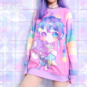 Puede incluir: Una sudadera rosa con un gran dibujo animado de un personaje con pelo azul y morado, una corona y un conejito morado. Las mangas son de rayas de colores arco&iacute;ris. El nombre de la tienda Etsy "merbunnybaby.etsy.com" es visible.