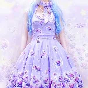 May include: A lavender halter dress with a rose and moon print. The dress features a full skirt and a bow at the neckline. The design includes roses, moons, and stars. The dress is a light purple color.