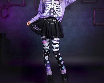May include: A lavender long-sleeve sweatshirt with a white skeleton ribcage print and heart accents, paired with a black pleated skirt featuring a silver chain and the text "Merbunny BABY", and black leggings with a white skeleton and heart pattern.