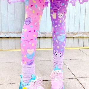 May include: Leggings with a pink and purple color scheme, decorated with heart-shaped candies and sprinkles. The leggings are paired with pink sneakers with blue soles and white laces. The outfit is completed with a ruffled skirt.