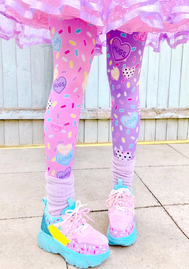 May include: Leggings with a pink and purple color scheme, decorated with heart-shaped candies and sprinkles. The leggings are paired with pink sneakers with blue soles and white laces. The outfit is completed with a ruffled skirt.