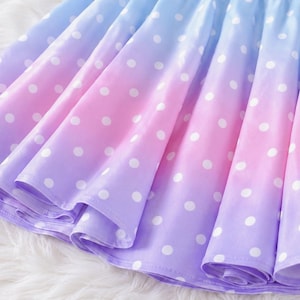 May include: A pleated skirt featuring a gradient color pattern that transitions from light blue at the top to pink in the middle and purple at the bottom. The entire surface of the skirt is covered in a repeating pattern of small white polka dots.
