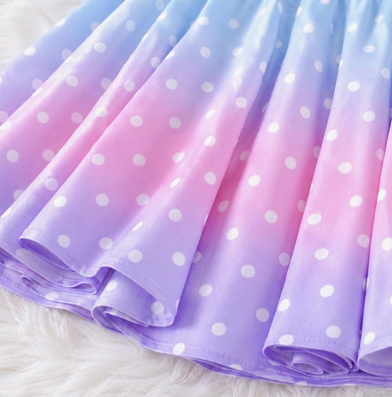 May include: A pleated skirt featuring a gradient color pattern that transitions from light blue at the top to pink in the middle and purple at the bottom. The entire surface of the skirt is covered in a repeating pattern of small white polka dots.