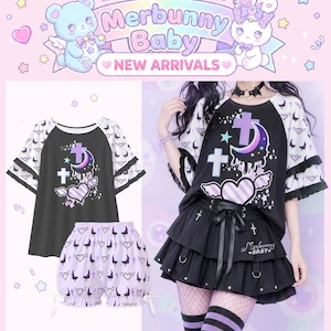 May include: A black and white raglan t-shirt with ruffled sleeves and a graphic print of a purple crescent moon, a cross, and a winged heart, paired with light purple shorts featuring a repeating pattern of moons, hearts, and crosses.