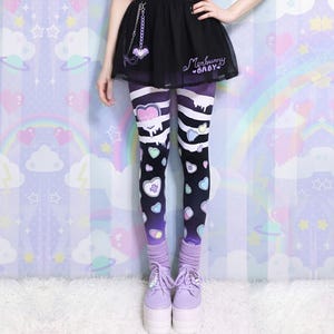 May include: Black and purple leggings with a heart and drip design, accented with pastel hearts and medical symbols. The leggings feature white stripes and a gradient effect. The outfit includes a black skirt with the text "Merbunny Baby" and lavender platform shoes.