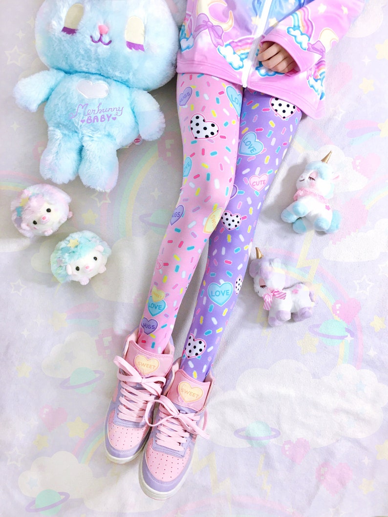 May include: A pair of pink and purple leggings with a heart and sprinkle pattern. The leggings are paired with pink and purple high-top sneakers with the word "Sweet" on the tongue. A blue plush bunny and unicorn are also in the image.