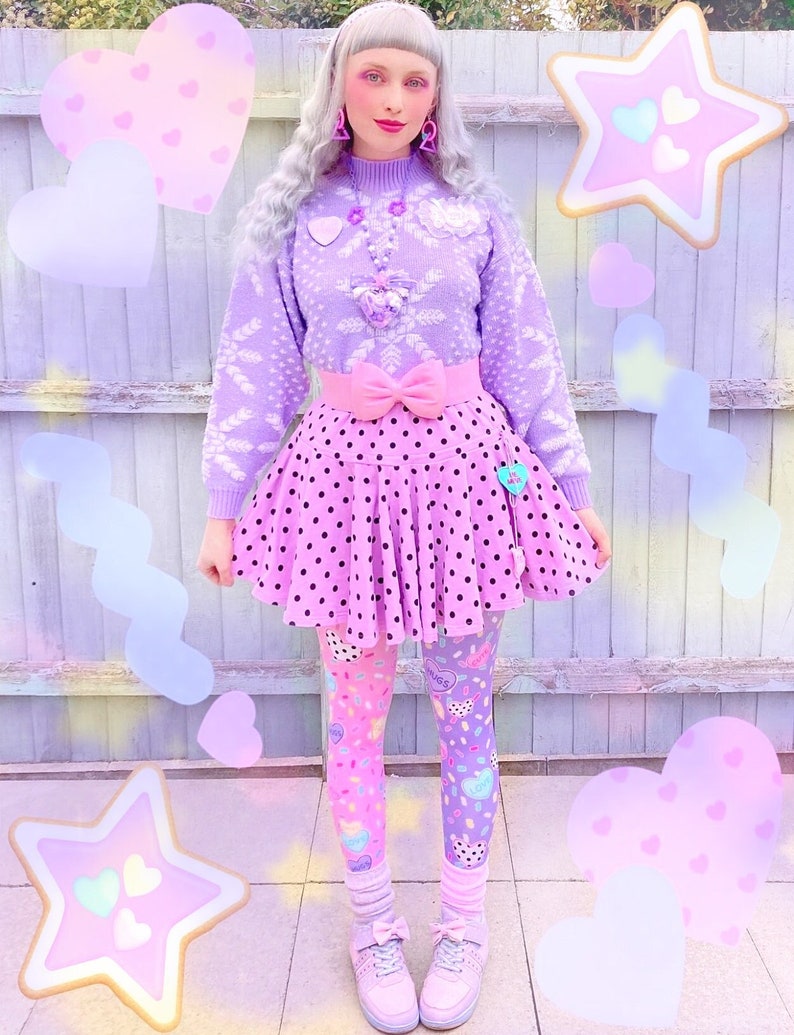 May include: A pastel-themed outfit featuring a lavender sweater with snowflake patterns, a pink polka-dot skirt, and color-blocked leggings. The ensemble includes a pink bow belt, matching shoes, and decorative accessories. The overall aesthetic is whimsical and playful.