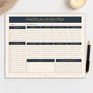May include: A weekly planner with the text "Find Peace in the Plan" in navy blue. The planner includes sections for priorities, to-do lists, and daily schedules. A gold pen rests on the right side of the planner.