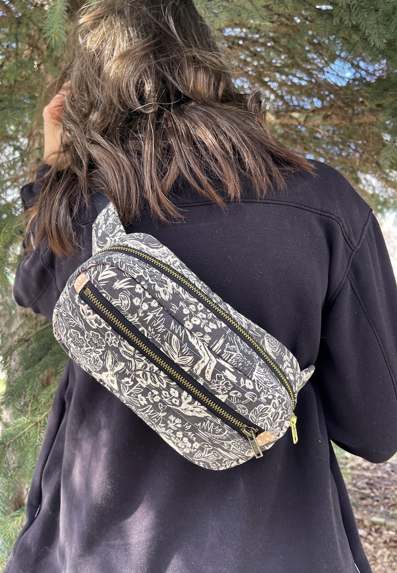 May include: A black and white patterned fanny pack with a zipper closure. The fanny pack is worn across the body.