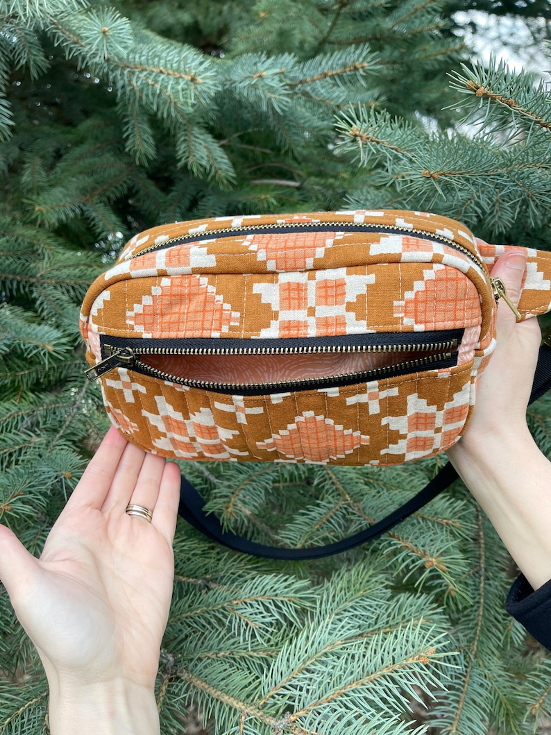 May include: A brown and orange quilted fabric fanny pack with a black strap and a gold zipper. The bag has a geometric pattern.
