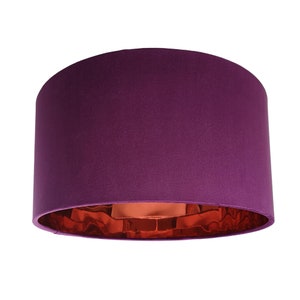 May include: A cylindrical lampshade in a deep purple colour. The interior has a metallic copper finish, creating a contrast. The lampshade is designed to be mounted on a lamp base.
