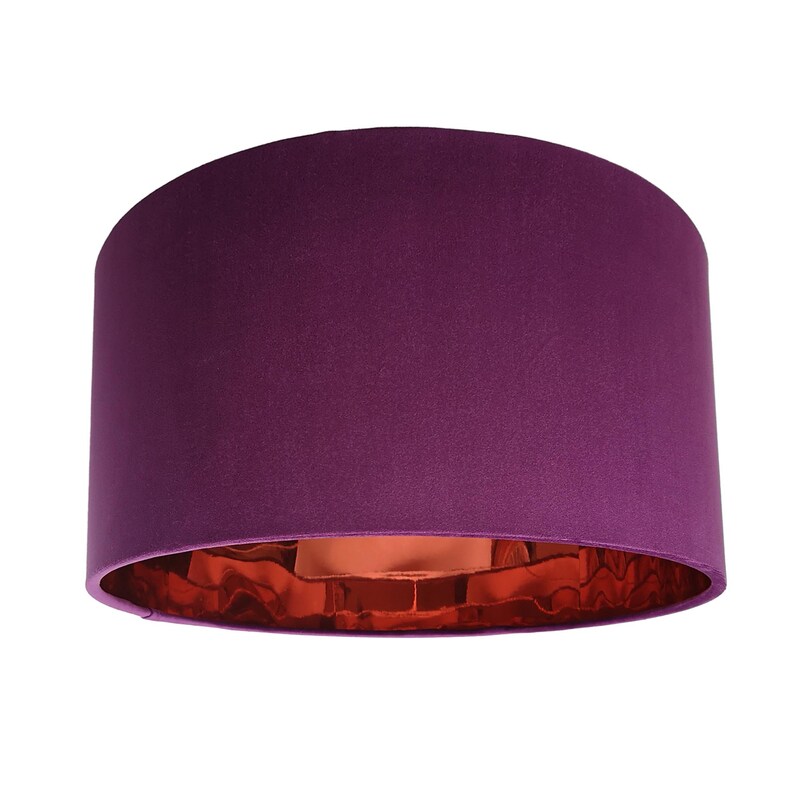 May include: A cylindrical lampshade in a deep purple colour. The interior has a metallic copper finish, creating a contrast. The lampshade is designed to be mounted on a lamp base.