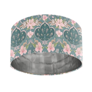 May include: A teal lampshade with a repeating pattern of pink flowers, tigers, and monkeys. The interior is silver. The design includes peacock feather shapes and floral elements, creating a whimsical and decorative aesthetic.