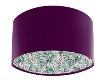 May include: A cylindrical lampshade in a deep purple hue. The interior is decorated with a tropical palm leaf design in green on a pale pink backdrop. The lampshade is designed to diffuse light.
