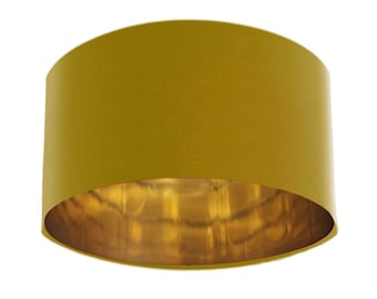 May include: A round, mustard yellow lampshade with a gold interior. The lampshade is made of fabric and has a smooth, even texture.