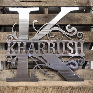 May include: Metal monogram with the letter K and the last name "KHARBUSH" in a decorative font. The letter K is adorned with intricate scrollwork.