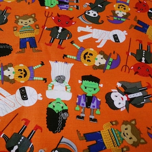 May include: Orange fabric with a repeating pattern of various Halloween characters, including a werewolf, a vampire, a ghost, a Frankenstein, a witch, and a devil. The characters are all cartoonish and have friendly expressions.