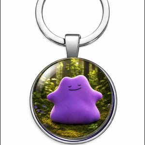 Könnte beinhalten: Ein runder Metallschlüsselanhänger mit einem Glaskabochon-Einsatz. Der Einsatz zeigt ein violettes, amorphes, klumpenartiges Wesen mit einem einfachen Strichgesicht, platziert in einer sonnendurchfluteten Waldumgebung mit grünem Moos und Farnen.