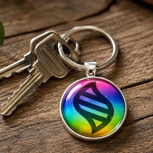 May include: A circular metal keychain featuring a vibrant rainbow gradient background with a black stylized DNA-like helix symbol in the center. The keychain is attached to a silver-toned metal split ring that holds two standard silver house keys.