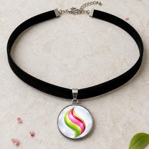 May include: A black velvet choker necklace featuring a round silver-toned pendant. The pendant contains a circular graphic with a swirling, abstract design in vibrant lime green and hot pink colours against a white background, secured by a metal clasp.