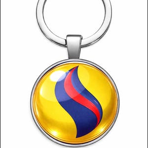 Puede incluir: Un llavero redondo con fondo amarillo y un diseño de llama azul y roja. El colgante tiene un marco de metal plateado y un llavero plateado.